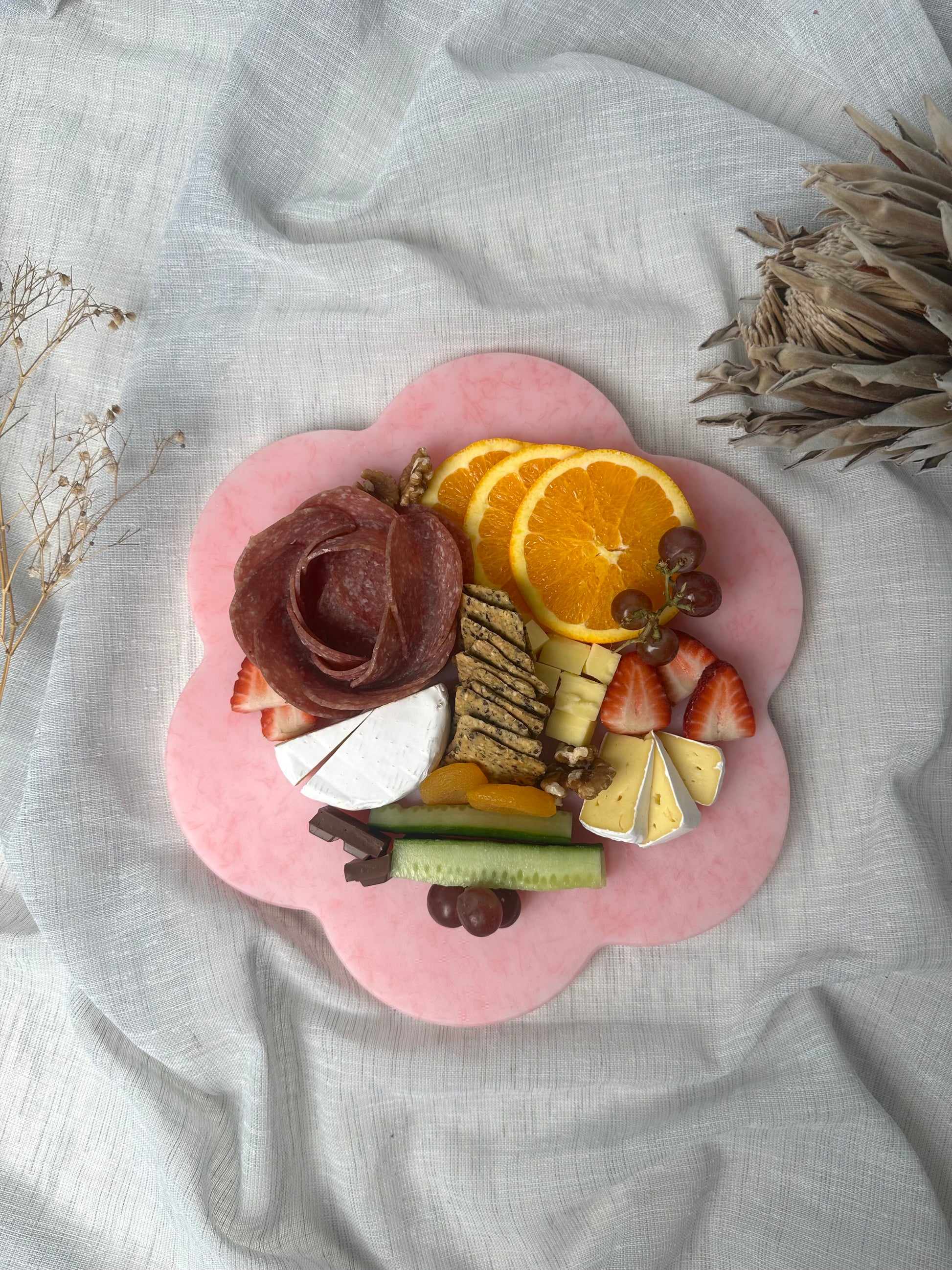 Pink flower shaped platter of assorted foods including fruits, cheese, and meats.