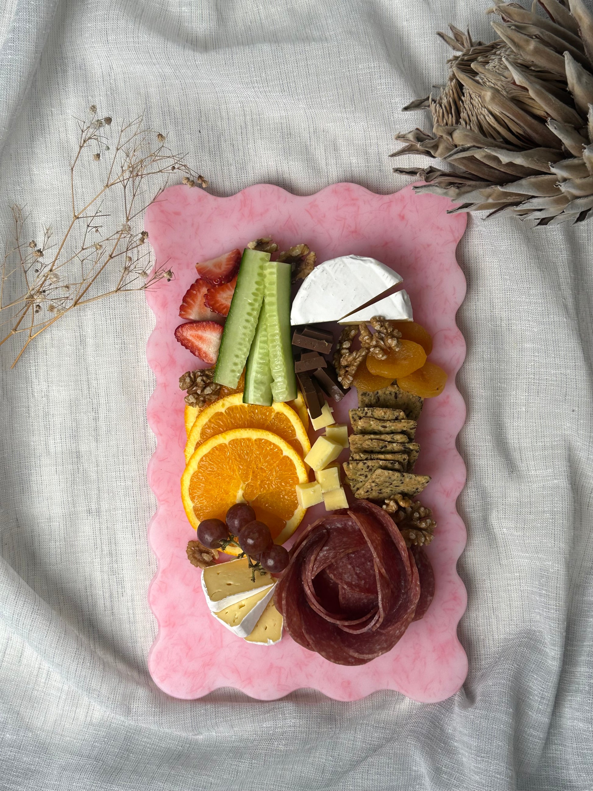 Pink charcuterie board with assorted food items including fruits, cheese, and meats.
