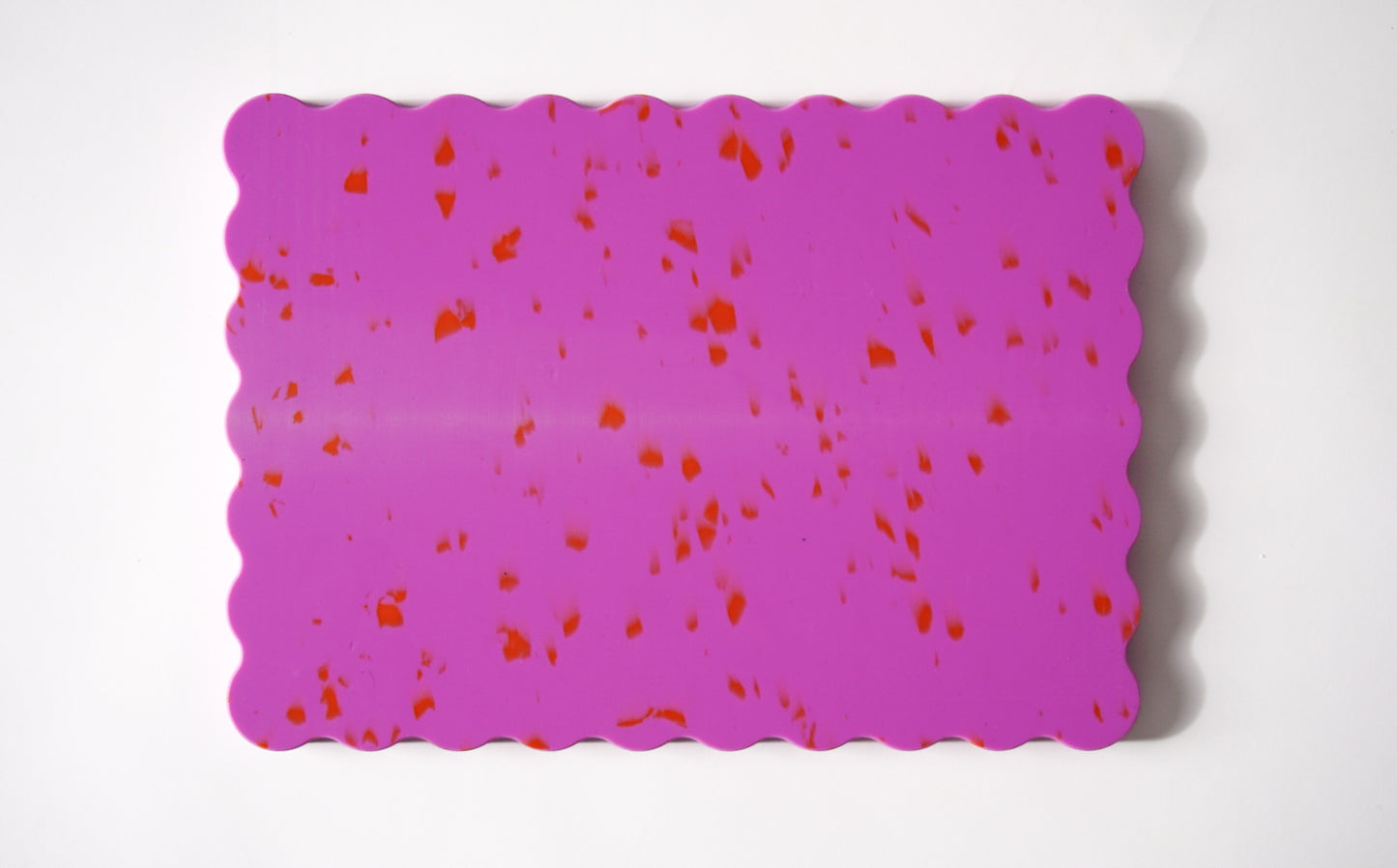 Pink wavy chopping board with orange speckles.