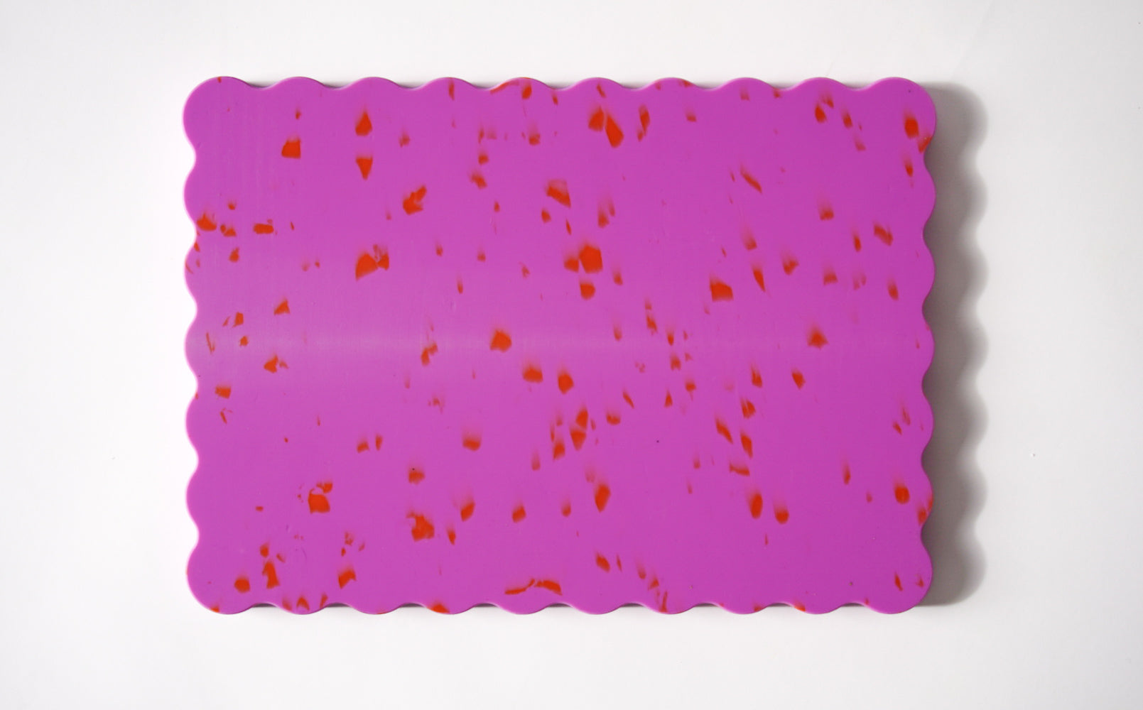 Pink wavy chopping board with orange speckles.