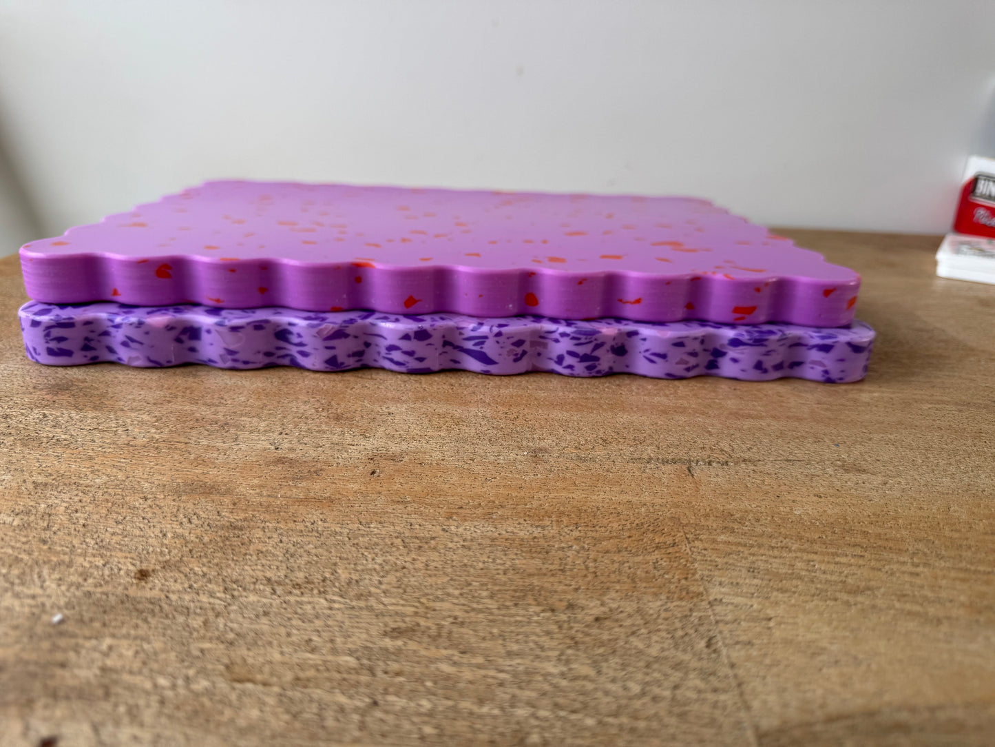 Pink wavy chopping board with orange speckles sitting on top of purple wavy chopping board