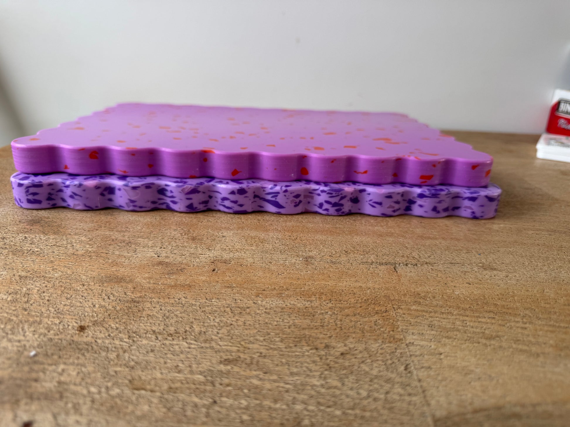 Pink wavy chopping board with orange speckles sitting on top of purple wavy chopping board