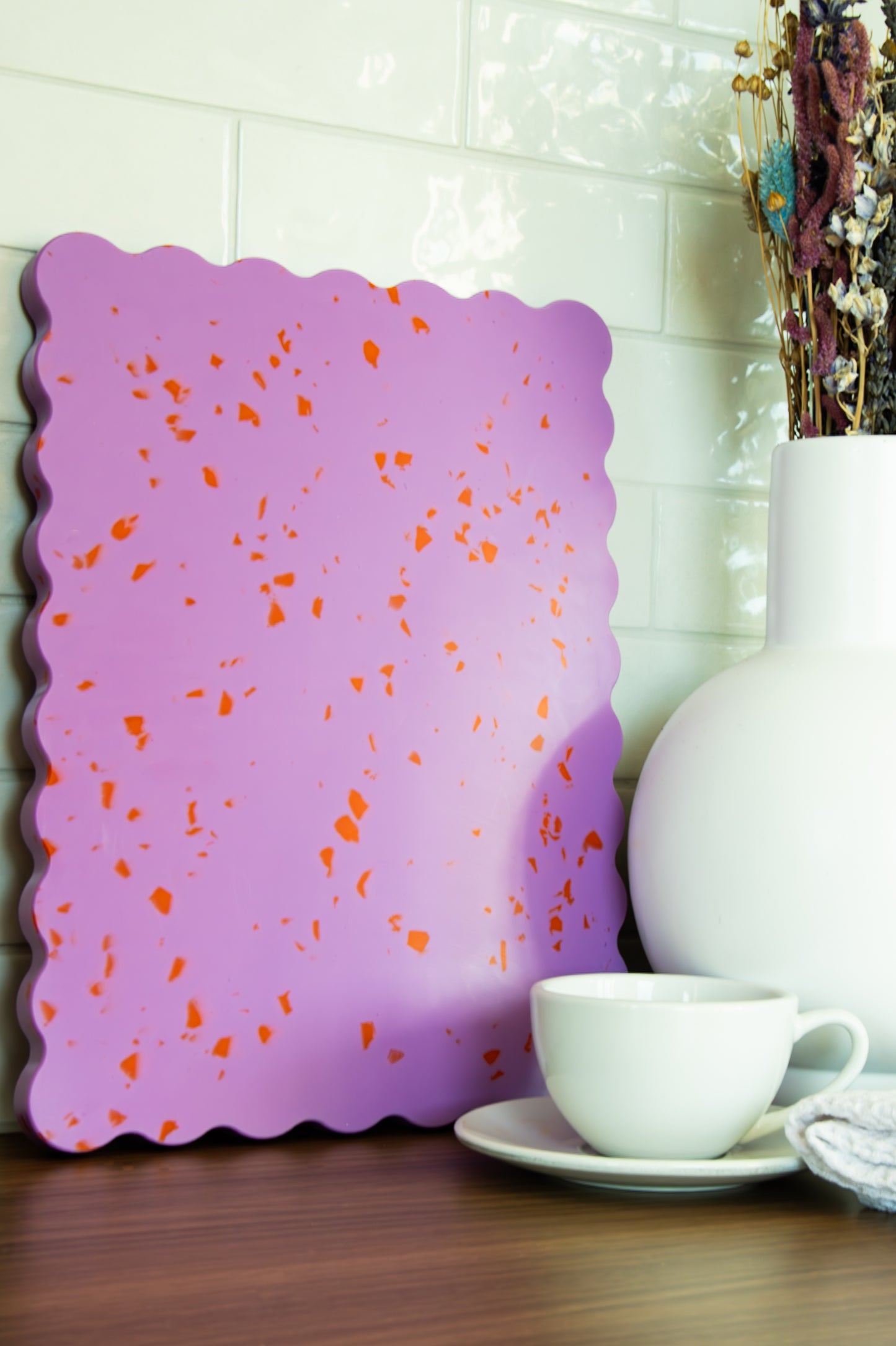 Pink wavy chopping board with orange speckles on table.