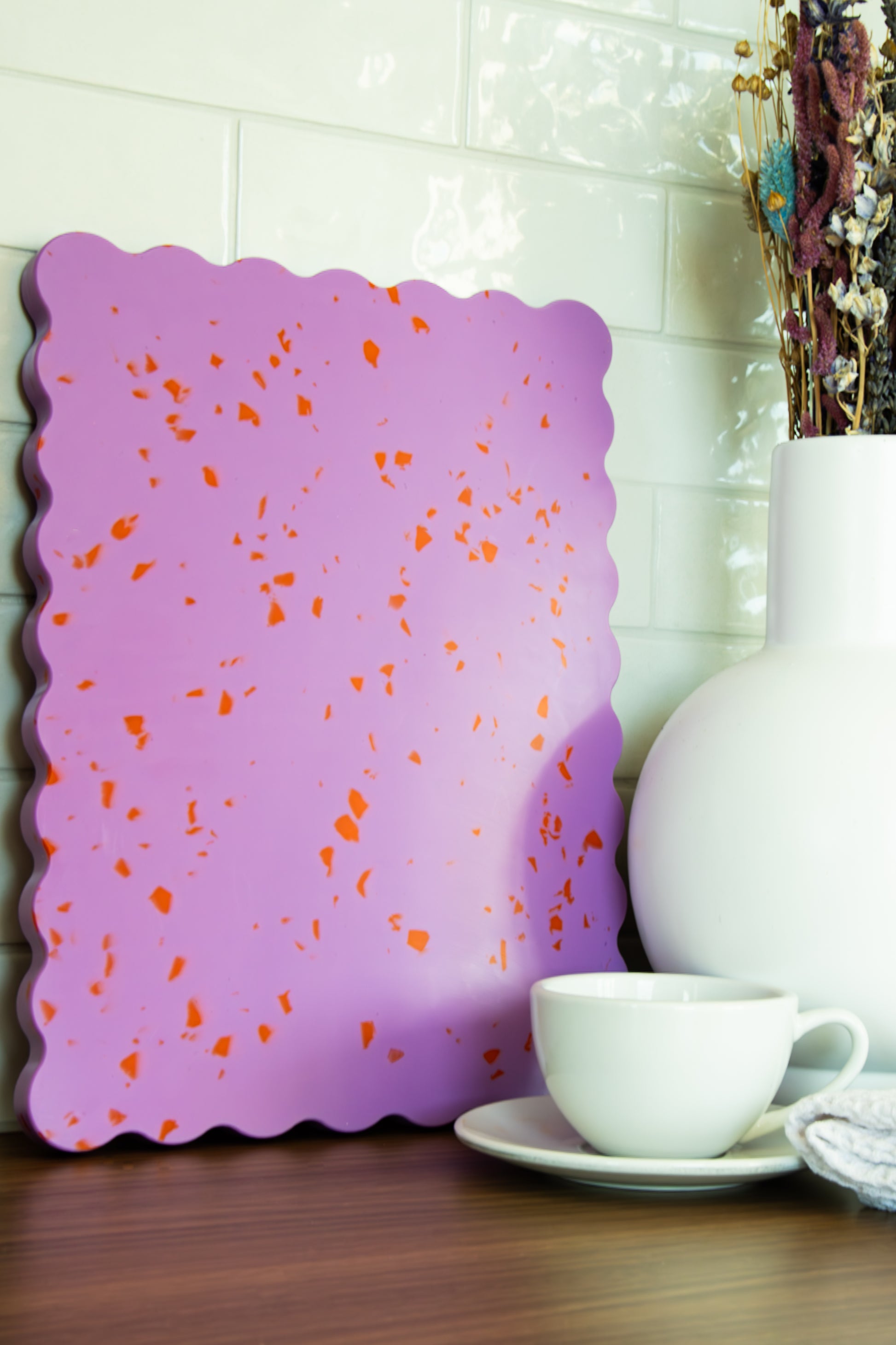 Pink wavy chopping board with orange speckles on table.