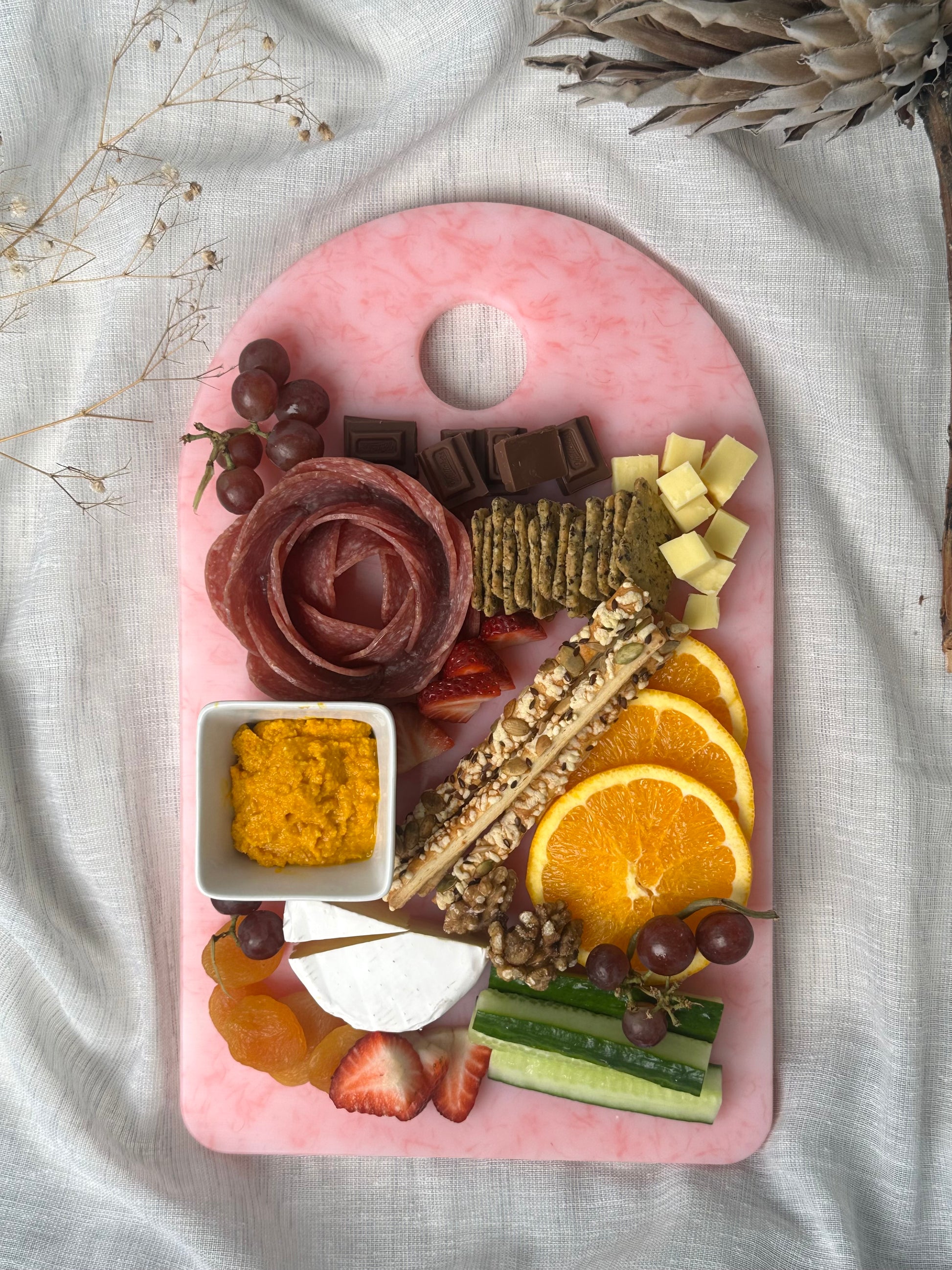 Pink platter with assorted snacks including fruits, cheese, and crackers