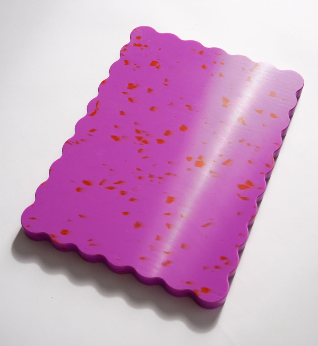 Pink wavy chopping board with orange speckles.